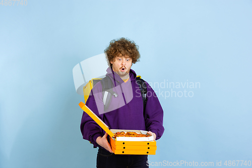 Image of Contacless delivery service during quarantine. Man delivers food and shopping bags during insulation. Emotions of deliveryman isolated on blue background.