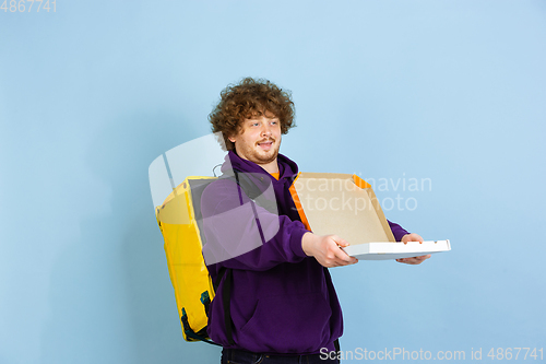 Image of Contacless delivery service during quarantine. Man delivers food and shopping bags during insulation. Emotions of deliveryman isolated on blue background.