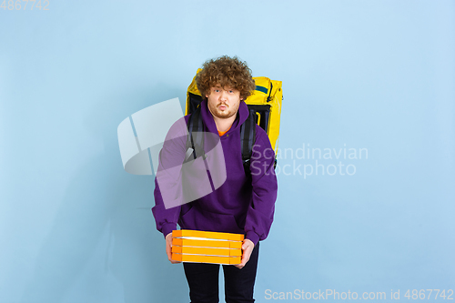 Image of Contacless delivery service during quarantine. Man delivers food and shopping bags during insulation. Emotions of deliveryman isolated on blue background.