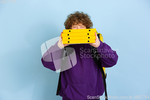 Image of Contacless delivery service during quarantine. Man delivers food and shopping bags during insulation. Emotions of deliveryman isolated on blue background.