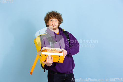 Image of Contacless delivery service during quarantine. Man delivers food and shopping bags during insulation. Emotions of deliveryman isolated on blue background.