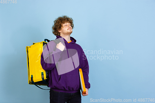 Image of Contacless delivery service during quarantine. Man delivers food and shopping bags during insulation. Emotions of deliveryman isolated on blue background.