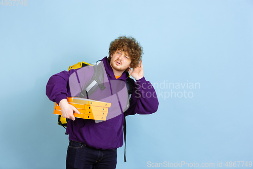 Image of Contacless delivery service during quarantine. Man delivers food and shopping bags during insulation. Emotions of deliveryman isolated on blue background.