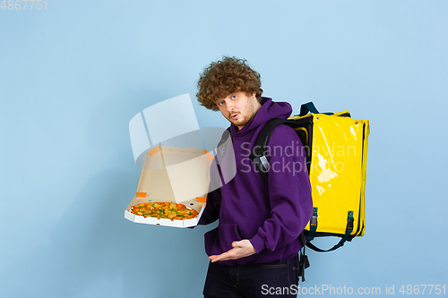 Image of Contacless delivery service during quarantine. Man delivers food and shopping bags during insulation. Emotions of deliveryman isolated on blue background.