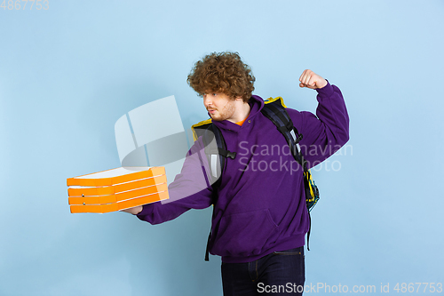 Image of Contacless delivery service during quarantine. Man delivers food and shopping bags during insulation. Emotions of deliveryman isolated on blue background.