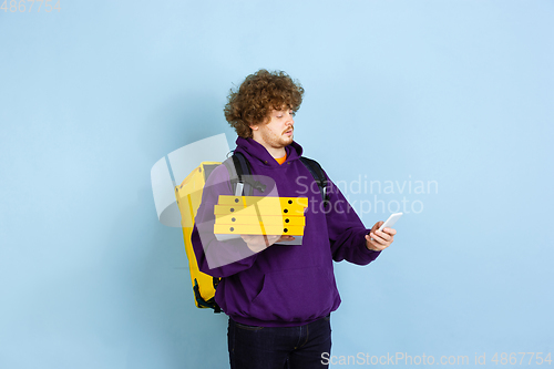 Image of Contacless delivery service during quarantine. Man delivers food and shopping bags during insulation. Emotions of deliveryman isolated on blue background.