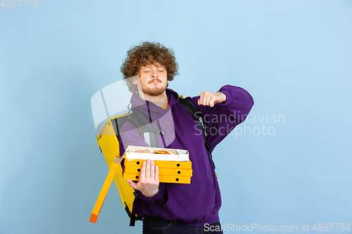 Image of Contacless delivery service during quarantine. Man delivers food and shopping bags during insulation. Emotions of deliveryman isolated on blue background.