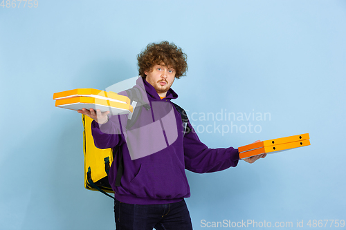 Image of Contacless delivery service during quarantine. Man delivers food and shopping bags during insulation. Emotions of deliveryman isolated on blue background.