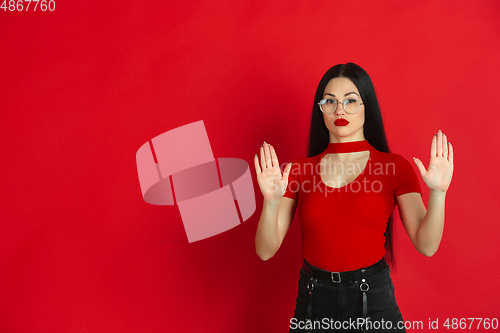 Image of Caucasian young woman\'s monochrome portrait on red studio background, emotional and expressive