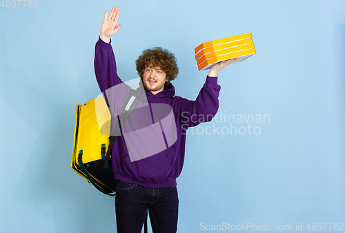 Image of Contacless delivery service during quarantine. Man delivers food and shopping bags during insulation. Emotions of deliveryman isolated on blue background.