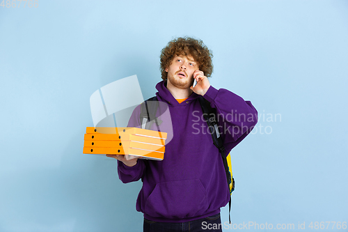 Image of Contacless delivery service during quarantine. Man delivers food and shopping bags during insulation. Emotions of deliveryman isolated on blue background.