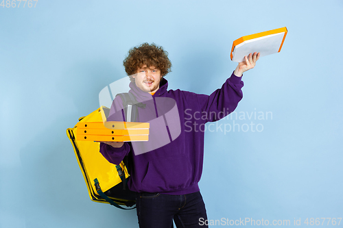 Image of Contacless delivery service during quarantine. Man delivers food and shopping bags during insulation. Emotions of deliveryman isolated on blue background.