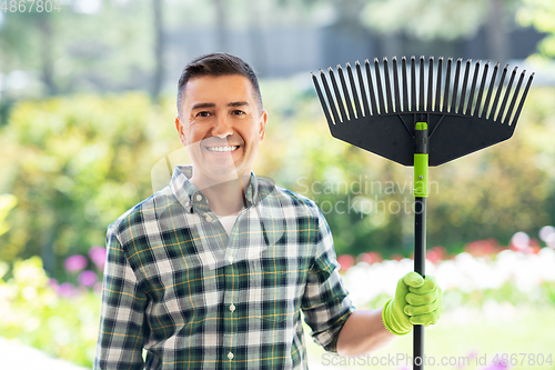 Image of happy middle-aged man with leaf rake at garden