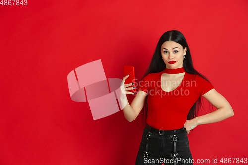 Image of Caucasian young woman\'s monochrome portrait on red studio background, emotional and expressive