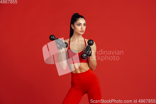 Image of Beautiful young female athlete practicing on red studio background, monochrome portrait