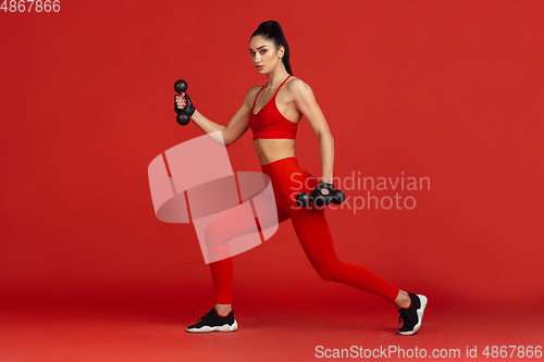 Image of Beautiful young female athlete practicing on red studio background, monochrome portrait