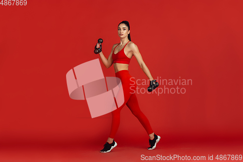 Image of Beautiful young female athlete practicing on red studio background, monochrome portrait