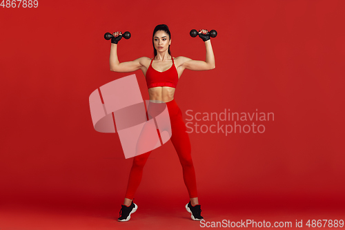 Image of Beautiful young female athlete practicing on red studio background, monochrome portrait