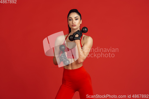 Image of Beautiful young female athlete practicing on red studio background, monochrome portrait