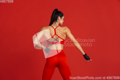 Image of Beautiful young female athlete practicing on red studio background, monochrome portrait