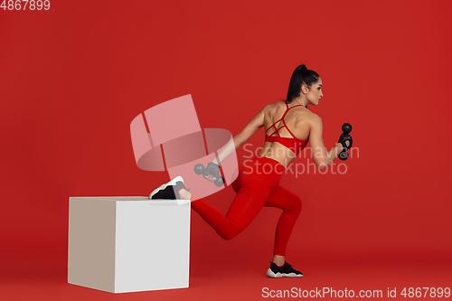 Image of Beautiful young female athlete practicing on red studio background, monochrome portrait