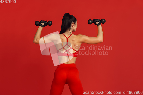 Image of Beautiful young female athlete practicing on red studio background, monochrome portrait