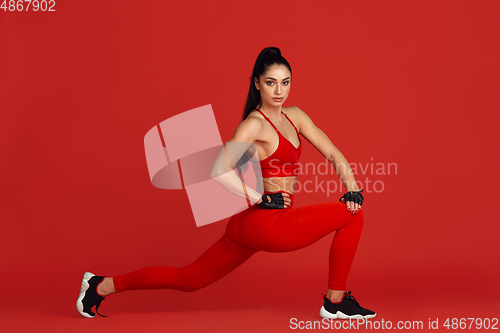 Image of Beautiful young female athlete practicing on red studio background, monochrome portrait