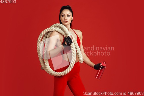 Image of Beautiful young female athlete practicing on red studio background, monochrome portrait