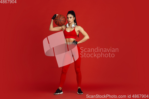 Image of Beautiful young female athlete practicing on red studio background, monochrome portrait