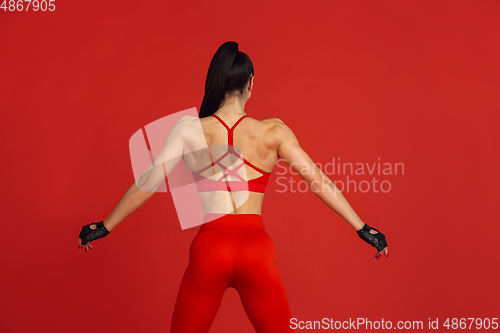 Image of Beautiful young female athlete practicing on red studio background, monochrome portrait