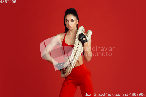 Image of Beautiful young female athlete practicing on red studio background, monochrome portrait