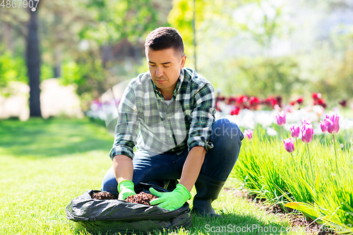 Image of man with soil in bag and flowers working at garden