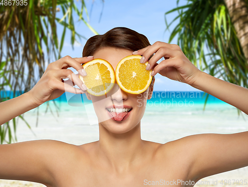 Image of woman making eye mask of orange slices on beach