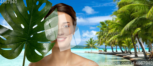 Image of young woman with green monstera leaf on beach