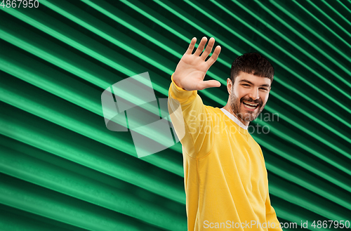 Image of smiling young man in yellow sweatshirt waving hand