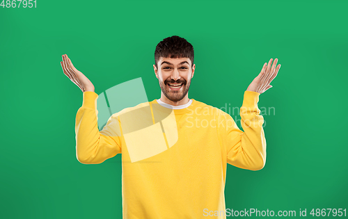 Image of happy man in yellow sweater shrugging over green