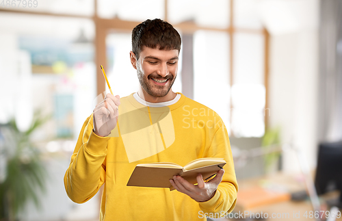 Image of happy man in yellow sweater with diary and pencil