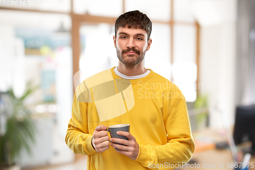 Image of displeased young man with coffee cup at office
