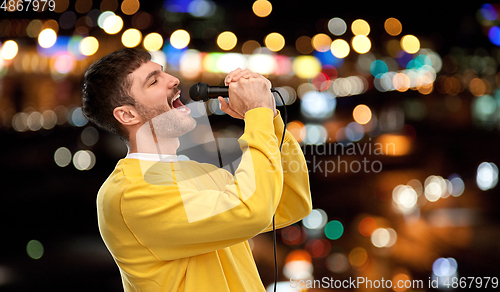 Image of man with microphone singing over night city lights