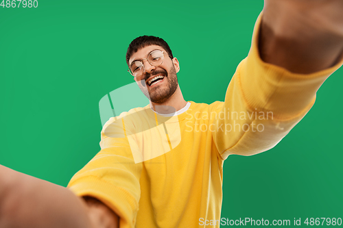 Image of happy young man in yellow sweatshirt making selfie