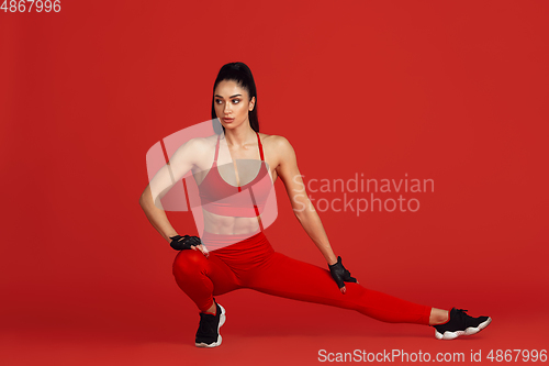 Image of Beautiful young female athlete practicing on red studio background, monochrome portrait