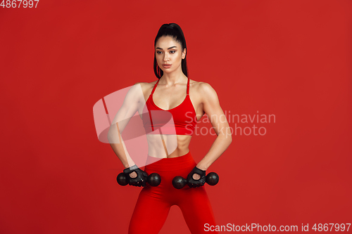 Image of Beautiful young female athlete practicing on red studio background, monochrome portrait