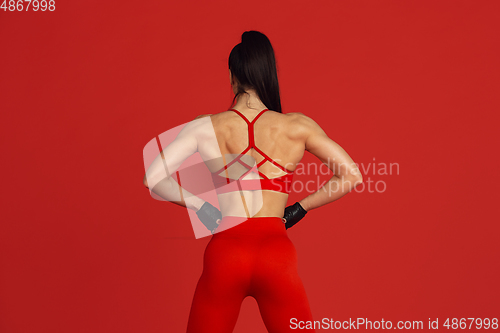 Image of Beautiful young female athlete practicing on red studio background, monochrome portrait