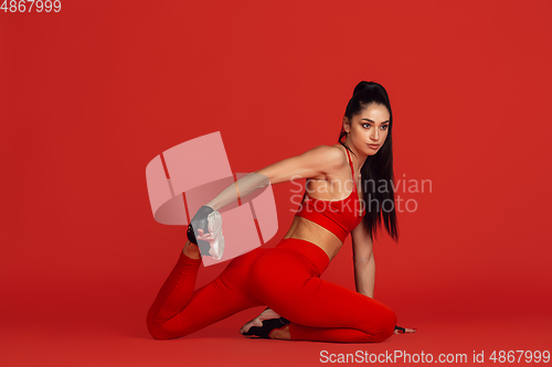 Image of Beautiful young female athlete practicing on red studio background, monochrome portrait