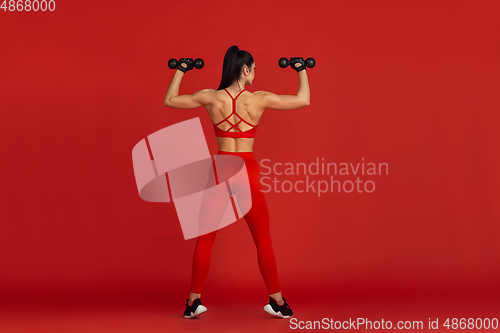 Image of Beautiful young female athlete practicing on red studio background, monochrome portrait