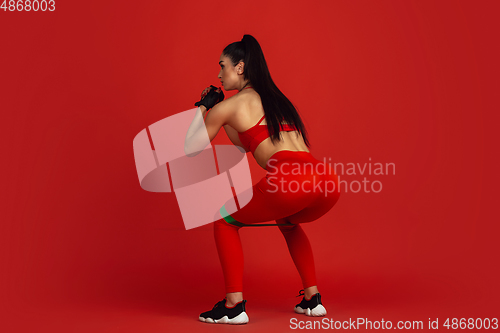 Image of Beautiful young female athlete practicing on red studio background, monochrome portrait