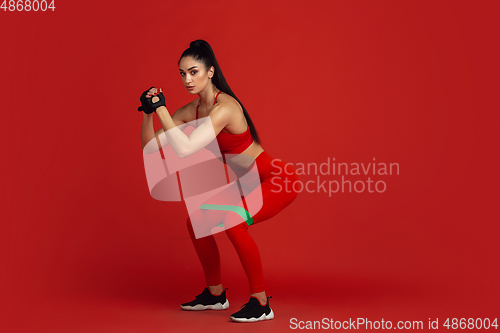 Image of Beautiful young female athlete practicing on red studio background, monochrome portrait