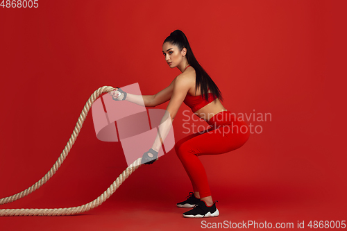 Image of Beautiful young female athlete practicing on red studio background, monochrome portrait