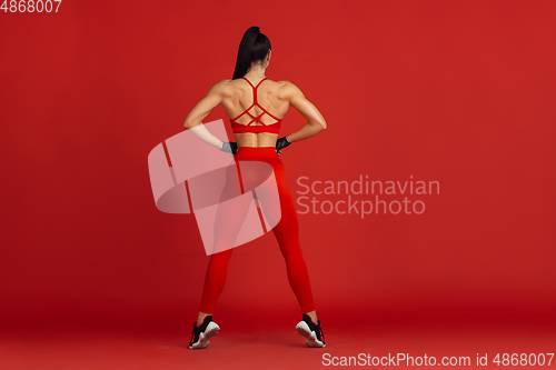 Image of Beautiful young female athlete practicing on red studio background, monochrome portrait