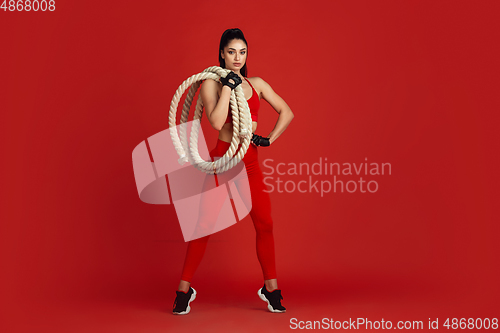 Image of Beautiful young female athlete practicing on red studio background, monochrome portrait